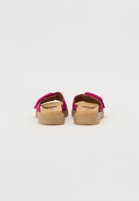 Fuchsiaslitna skor med en strukturerad ovandel och en formad beige sula. Har ett band över toppen för en säker passform.