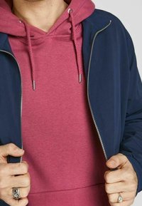 Námořnická bomber bunda se zipem vpředu přes růžovou mikinu s šňůrkami. Hladká látka s žebrovanými akcenty a stříbrnými kovovými prvky.