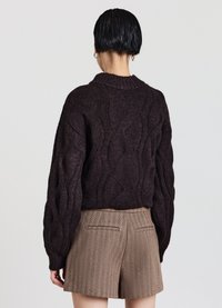Maglione a trecce di colore marrone scuro con collo alto, maniche lunghe e dettagli a coste, abbinato a pantaloncini marroni strutturati.