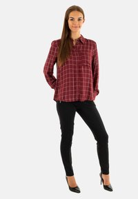 Camicia a quadretti bordeaux con colletto button-down e taschino sul petto, abbinata a pantaloni neri slim-fit e décolleté neri a punta.