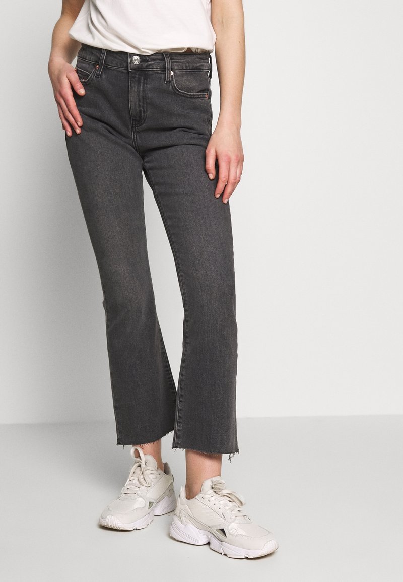 Mörkgrå avklippta jeans i denim med fransad nederkant och framfickor, kombinerat med vita sportskor.