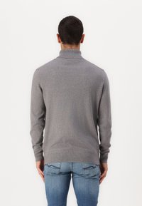 Grijze, gebreide turtleneck trui met lange mouwen, naadloos ontwerp, geribde kraag en zoom, gedragen met blauwe spijkerbroek.