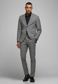 Grau Anzug mit taillierter Passform, mit zwei Knöpfen und Revers, kombiniert mit einem schwarzen Hemd und schwarzen eleganten Schuhen.
