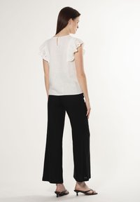 Blusa bianca in lino con maniche in pizzo arricciato e dettagli a oblò sul retro. Abbinata a pantaloni neri larghi e sandali neri minimal.