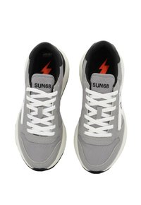 Sneaker in tessuto grigio con lacci bianchi, caratterizzate da un logo a saetta nero e rosso, e una suola color crema a contrasto. Design minimalista, senza motivi.