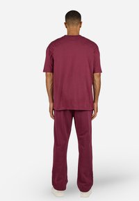 Bordeaux-rotes Zweiteiler-Outfit, bestehend aus einem kurzärmeligen Hemd und lockeren Hosen, gefertigt aus einem weichen Stoff mit glatter Textur.