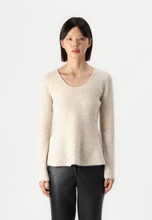 Beige ribbestrikket genser med rund hals, lange ermer og peplumform, laget av et mykt, strukturert stoff. Kombinert med svarte bukser.