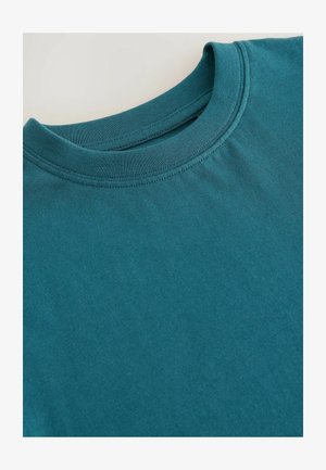 Camiseta de algodón color teal con cuello redondo. Textura suave y mangas cortas, con dobladillo cosido y sin gráficos ni patrones visibles.