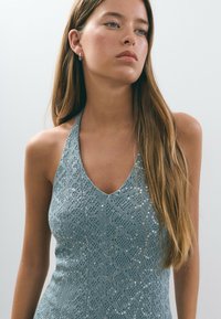 Haut halter en dentelle bleu clair avec un décolleté en V profond, des motifs complexes et des paillettes subtiles pour ajouter de la texture et de l'éclat.