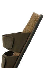 Sandal in suede verde con soletta in sughero, suola esterna con texture e bordatura marrone a contrasto. Presenta due cinturini regolabili.