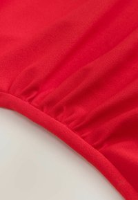 Gros plan d’un tissu rouge avec une couture élastique froncée créant de légers plis le long du bord.