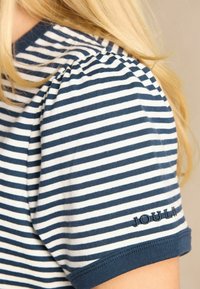 Röstripeline T-särk, millel on tumesinised ja valged horisontaalsed triibud, volangvarrukad ning tumesinise värviga välja broderitud "JOULES" logo varrukas. 