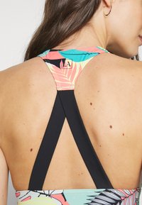 Multicolored sports top featuring a floral pattern with pink, teal, and black design, and black crisscross straps at the back.