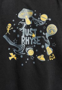 Svart stoff med et fargerikt grafisk design som viser aliens, sopper, stjerner, planeter, en rakett, og teksten "JUST RHYSE" i grått og gult.