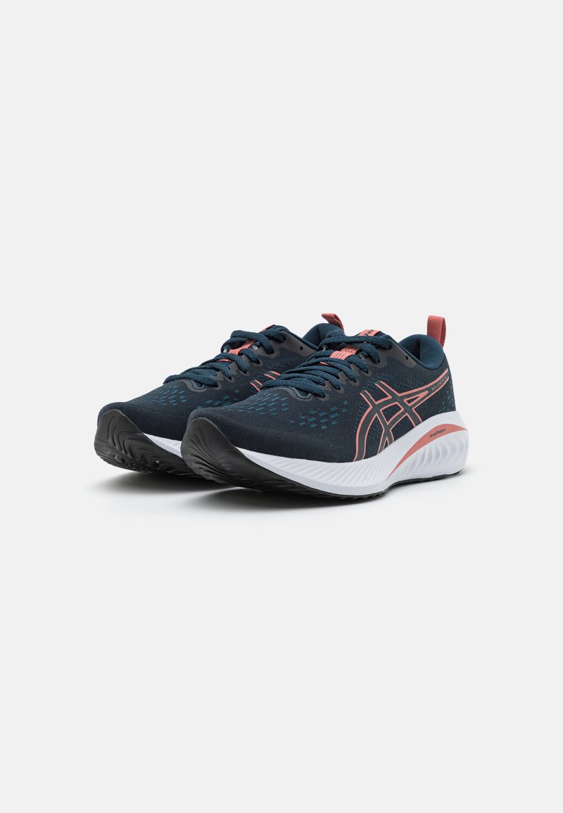 Une paire de chaussures de course bleu marine et corail avec des semelles blanches, des lacets et un logo de marque, présentée en angle sur un fond blanc.