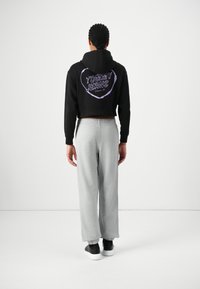 Zwarte crop hoodie met een paarse "TOMMY JEANS" logo op de achterkant, gecombineerd met grijze sweatpants en zwarte sneakers. Glad stofgevoel.