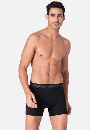 Čierne boxerky zo 100% bavlny s šedým elastickým pásom, na ktorom sa nachádza názov značky "MUCHACHO MALO" tučným písmom.