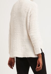 Pull crème texturé à coupe ample, col rond, manches longues et fentes latérales, confectionné dans un matériau doux et duveteux.