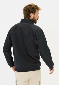 Marineblauwe jas met een hoge kraag, ribbelmanchetten en een ribbelzoom. Het materiaal lijkt glad met een gestructureerde achterkant, een getailleerd ontwerp en minimale details.