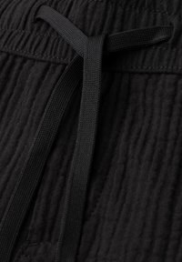 Pantalon en tissu noir texturé avec une taille élastique et un cordon plat noué au centre devant.