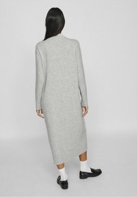 Longue robe grise en maille avec un col rond, des poignets côtelés et une coupe décontractée, associée à des mocassins noirs et des chaussettes blanches.