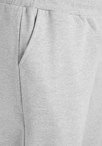 Sivi flis materijal s ravnim prednjim džepom i elastičnim pojasom. Mekana tekstura s glatkom i blago melirastom završnom obradom.