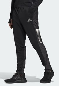 Svarta träningbyxor med slim fit, med glänsande svarta sidpaneler och tre vita ränder vid underbenet. Tillverkade av lätt material.