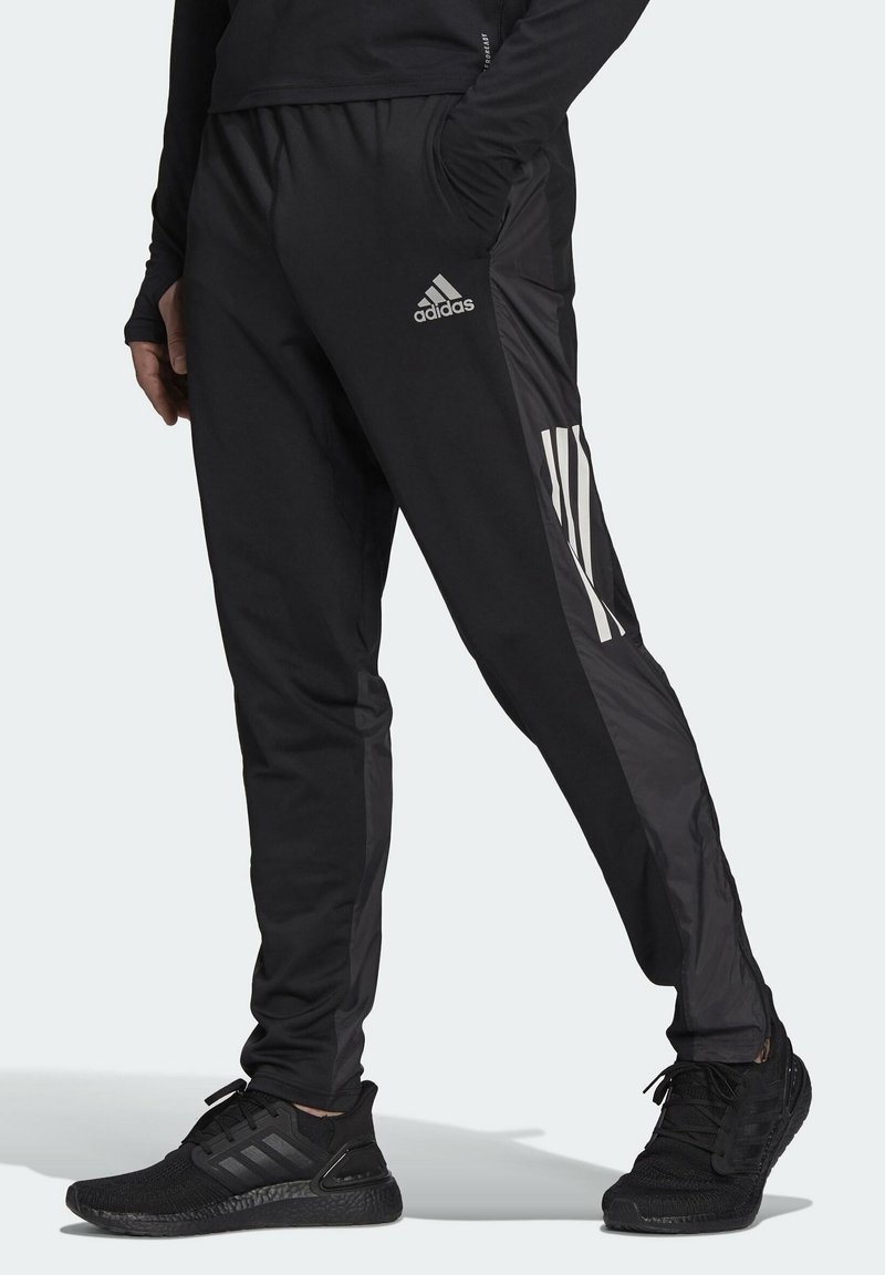 Svarta träningbyxor med slim fit, med glänsande svarta sidpaneler och tre vita ränder vid underbenet. Tillverkade av lätt material.