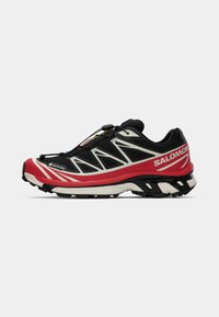 Schwarzer und roter Trailrunning-Schuh mit einer strukturierten Sohle, GORE-TEX-Branding und einem verstellbaren Schnürsystem. Schlankes Design mit weißen Akzenten.