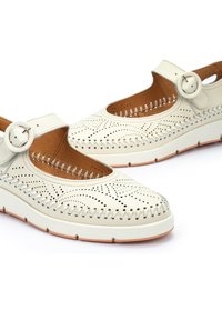 Chaussures en cuir blanc avec un bout rond, un design perforé et une sangle à boucle. Elles possèdent une semelle intérieure rembourrée et une semelle en caoutchouc surélevée.