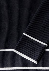 Marinblå ribbat striktyg med vita horisontella ränder. Har en texturerad yta och kontrasterande vit kant vid ärmsluten och nederkanten.