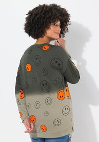 Camiseta de manga larga en verde oliva, con un degradado a beige claro, decorada con patrones de caritas sonrientes en negro y naranja.
