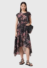 Abito nero a fiori con accenti rosa, caratterizzato da maniche corte e un orlo asimmetrico. Abbinato a una borsa a tracolla nera e sandali flat.