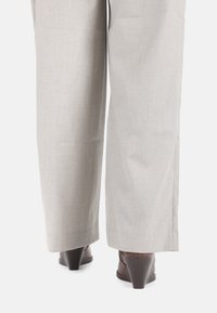 Pantalones de pierna ancha color gris claro con una textura suave y un ligero brillo, combinados con tacones de cuña marrones que presentan un diseño curvado y acentos texturizados.