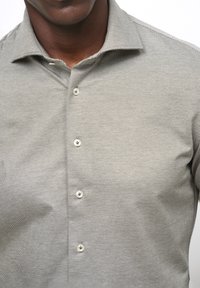 Knapplång skjorta i ett strukturerat, ljusgrått tyg med subtila vertikala ränder och fem dekorativa knappar längs knäppningen.