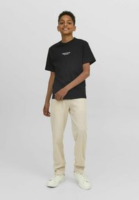 Camiseta de algodón negra de manga corta con un gráfico frontal. Combinada con pantalones beige y zapatillas blancas. Corte claro y relajado.