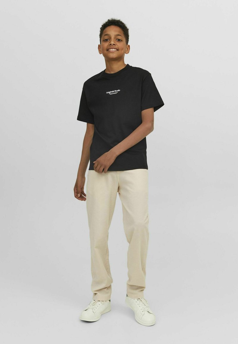 Camiseta de algodón negra de manga corta con un gráfico frontal. Combinada con pantalones beige y zapatillas blancas. Corte claro y relajado.
