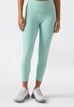 Miętowozielone, dopasowane legginsy sportowe z wysokim paskiem i bocznymi kieszeniami, zestawione z białymi butami sportowymi z szarymi akcentami.