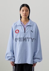 Light blue oversized jacket featuring a collar, PUMA logo, "FENTY" text, and a circular patch on the left side. Textured fabric, long sleeves.