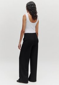 Zwarte wijde broek met een gladde, gestructureerde afwerking, gecombineerd met een witte, mouwloze tanktop met een lage rugdesign.