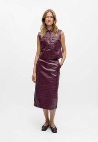 Chaleco corto de polipiel morado con bolsillos frontales, combinado con una falda lápiz larga a juego que presenta una textura de piel de cocodrilo.