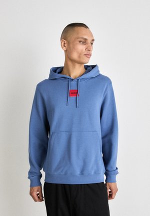 Blauwe pullover hoodie met voorzak en trekkoordcapuchon. Beschikt over een rood rechthoekig logo-patch in het midden van de borst. Zachte textuur.