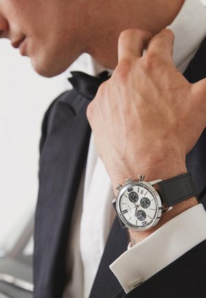 Silver and black chronograph watch with a white dial, featuring three subdials, stainless steel case, and a black leather band.