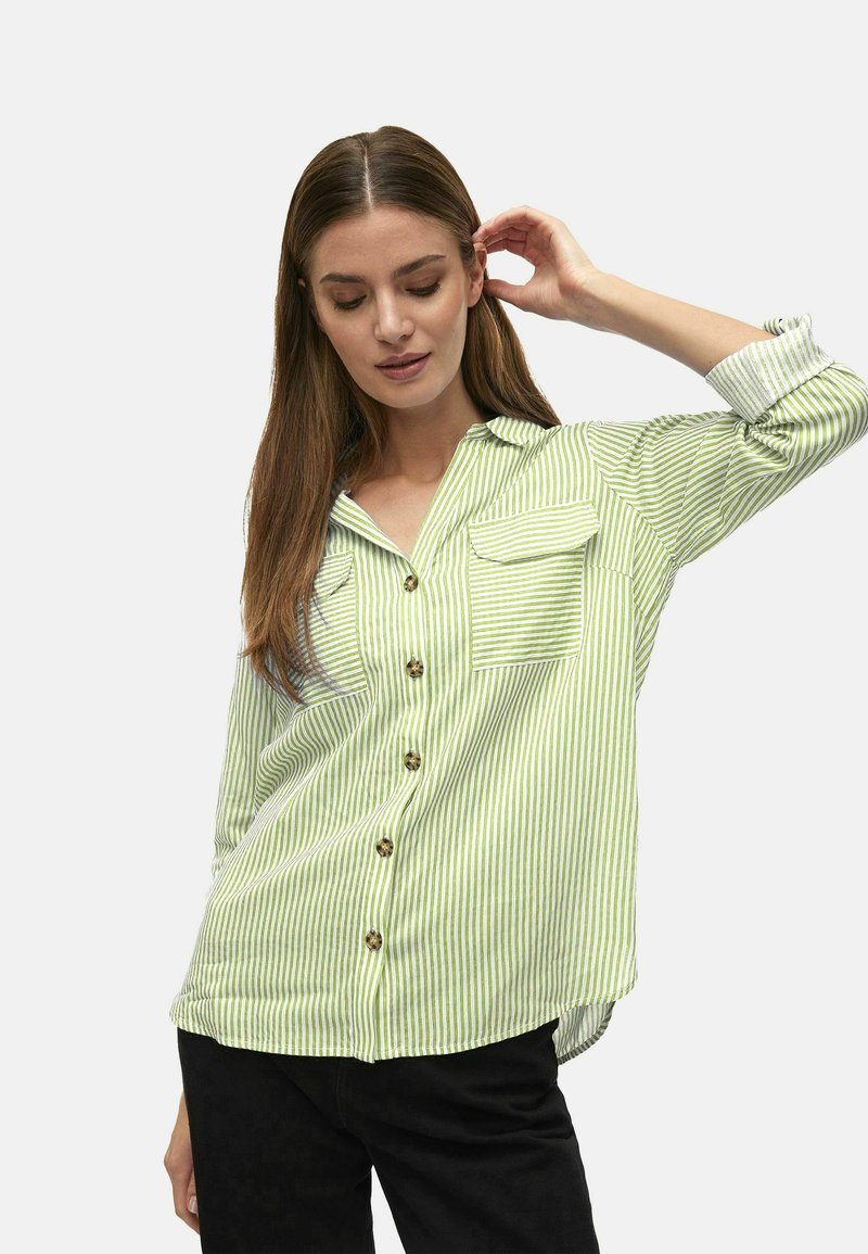 Camisa abotonada a rayas verdes y blancas, de tejido ligero, con dos bolsillos en el pecho y cuello. Mangas largas arremangadas hasta los codos.