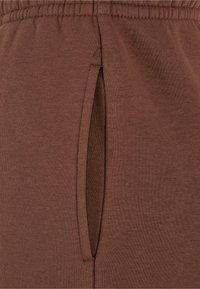 Bruine katoenen joggers met een zijzak met een gleufontwerp, elastische tailleband en een gladde textuur.