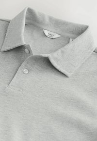 Polo de rayas en gris, fabricado en una mezcla de algodón, con una tapeta de botones, cuello y una textura suave. La etiqueta dice "NEXT Regular Fit."