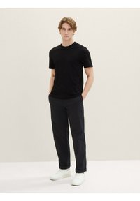 Black short-sleeve t-shirt paired with dark trousers and white sneakers. The t-shirt has a round neckline and a smooth texture.
