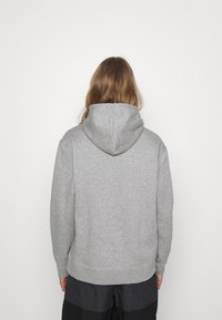 Šedá mikina s kapucí a šňůrkou, žebrované lemy u rukávů a spodního lemu. Hladká textura, volný střih a minimální detaily na zadní straně.