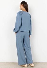 Conjunto de dos piezas de color azul claro que presenta una blusa de manga larga con detalles de encaje en la espalda y pantalones de pierna ancha, confeccionado con un material suave.