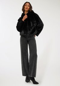 Czarna kurtka z futra syntetycznego z kapturem, w luźnym fasonie, z zapięciem na suwak z przodu. Zestawiona z czarnymi dżinsami o wysokim stanie, zdobionymi rozrzuconymi srebrnymi elementami dekoracyjnymi.